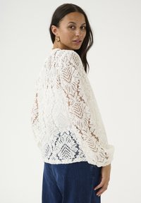 White lace blouse featuring intricate floral patterns, long sleeves, and a relaxed fit. Accented with a rounded neckline and soft texture.