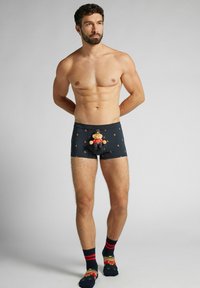 Czarne bokserki z wzorem, z kreskówkową postacią z przodu, o dopasowanym kroju. Model nosi paskowane skarpety i ma umięśnioną sylwetkę.