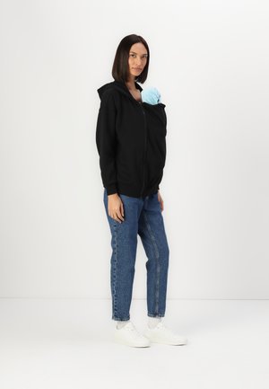 Zwarte zip-up hoodie met een voork pocket, gecombineerd met blauwe jeans en witte sneakers. Hoodie heeft een zachte textuur; bevat een lichtblauw item.