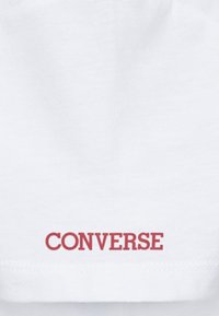 Biele bavlnené tričko s červeným logom "CONVERSE" potlačeným na prednej strane blízko lemu. Hladká textúra s klasikým okrúhlym výstrihom.