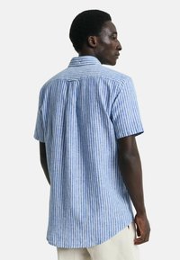 Camicia a maniche corte blu e bianca a righe con orlo curvo e dettaglio sul retro, realizzata in tessuto leggero.