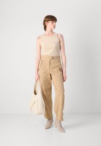 Beige toppi, khaki cargo-housut monilla taskuilla ja vaaleanbeige käsilaukku. Mallilla on päällä vaalean taupe-töppöset. Yksinkertainen muotoilu, pehmeät pinnat.