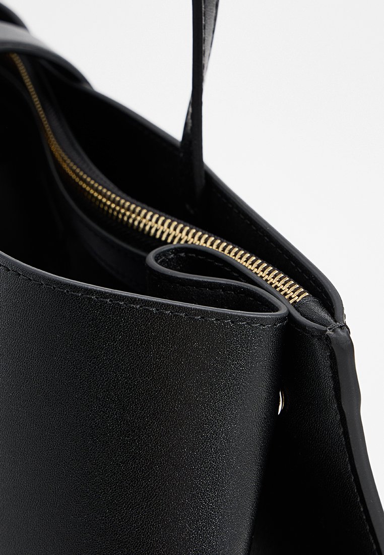 Sac à main en cuir noir avec fermeture éclair dorée. L'intérieur présente une doublure lisse et une poche courbe le long du bord du sac.