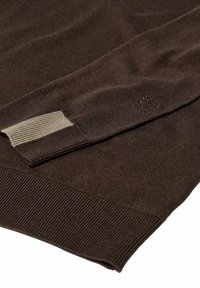 Brauner Pullover mit einer weichen Textur, ausgestattet mit gerippten Bündchen und einem hellen Taubentonstreifen. Dezente Logo-Stickerei nahe dem Bündchen.