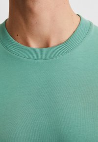 Miętowo-zielony sweter z okrągłym dekoltem, charakteryzujący się ribbowanym wykończeniem dekoltu i gładką teksturą, prezentujący proste, nieozdobione wzornictwo.