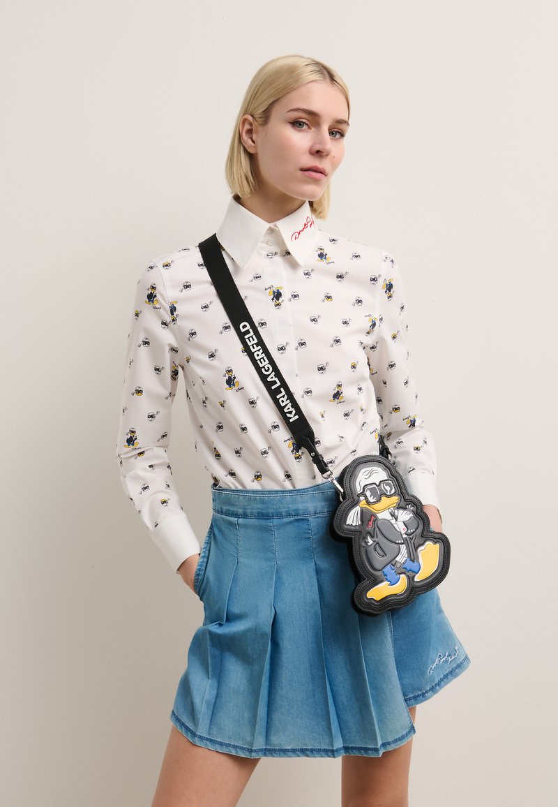 Camisa blanca con estampados de dibujos animados, de mangas largas y cuello con solapa, combinada con una falda plisada de mezclilla azul. Bandolera negra que lleva un bolso con forma de pingüino.