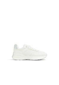 Zapatilla blanca de corte bajo con cierre de cordones, paneles texturizados, suela gruesa y acento metálico plateado en el talón, mostrada de lado sobre fondo blanco.