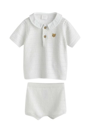 White knitted baby set with short-sleeve top featuring a collar, two wooden buttons, and a small teddy bear patch, plus matching shorts.