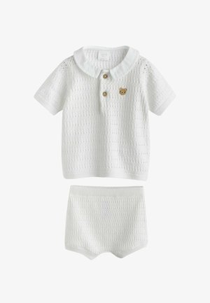 Ensemble bébé blanc en tricot avec un haut à manches courtes doté d'un col, de deux boutons en bois et d'un petit patch nounours, accompagné d'un short assorti.