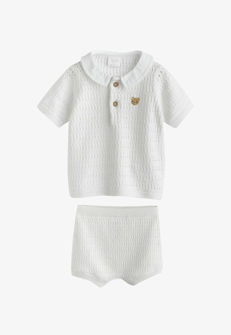 Ensemble bébé blanc en tricot avec un haut à manches courtes doté d'un col, de deux boutons en bois et d'un petit patch nounours, accompagné d'un short assorti.