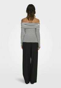 En sort-hvid stribet off-shoulder langærmet bluse parret med brede sorte bukser, der har en glat tekstur og en afslappet pasform.