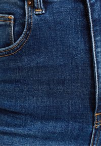 Jeans i denim i mörkblått med en slät yta, som har en framficka, orange sömnadsdetaljer och en metallknapp som accent.