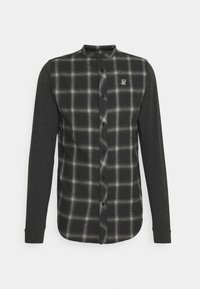 Camisa de manga larga a cuadros en negro y gris con un frente abotonado, mangas oscuras en contraste y un pequeño logo bordado en el pecho.