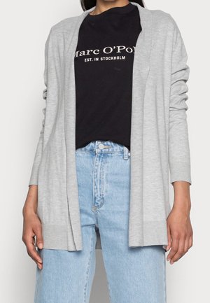 Cardigan grigio realizzato in morbido tessuto lavorato a maglia, design aperto sul davanti, maniche lunghe e polsini a coste, abbinato a una t-shirt nera con grafiche e jeans chiari.