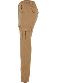 Pantalon cargo beige avec une ceinture élastique, un cordon de serrage, une poche latérale à rabat et un détail de poche avant cousue, présenté de profil.