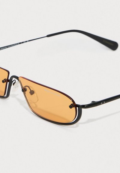Lunettes de soleil de style black metal avec des verres teintés orange, présentant une forme rectangulaire élégante et un design minimaliste. Marque notable sur la monture.