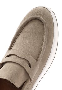 Beige suede loafer with a rounded toe and a strap across the upper. White rubber sole is visible at the base, indicating comfort and casual style.