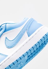 Låg vinkelvy av en vit och ljusblå Nike-sneaker som fokuserar på sidans swoosh-logotyp och den texturerade sulan.