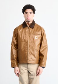 Giacca in bronzo con colletto in velluto a coste marrone, chiusura con zip frontale e tasche laterali. Il materiale ha una texture liscia e leggermente lucida.