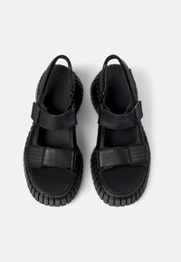 Black leather sandals with a rounded toe, adjustable straps, and a textured rubber sole. The design incorporates contrasting strap accents.