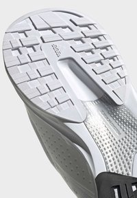 Suela de zapato deportivo con una superficie blanca texturizada, un patrón de agarre y un acento negro. Incluye un detalle del "Sistema de Torsión".