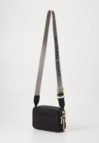 Melnās neilona plecu somas ar taisnstūra formu, zelta rāvējslēdzis un pelēks siksna ar "MICHAEL KORS" zīmolu. Gluda tekstūra.
