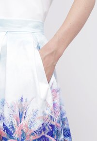 Une longue jupe bleu clair avec un imprimé de palmiers. Elle présente une taille haute et des poches latérales. Confectionnée dans un tissu lisse et léger.
