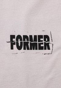 Μαύρο έντονο κείμενο "FORMER" τυπωμένο σε ανοιχτόχρωμο ύφασμα με φθαρμένο, παλαιωμένο εφέ γύρω από τις άκρες.