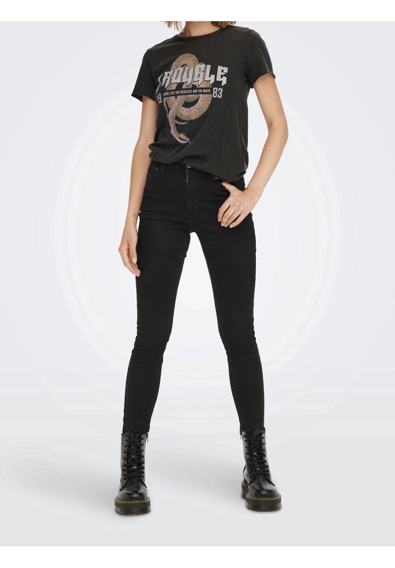 Camiseta gráfica negra con un diseño de serpiente y texto, combinada con jeans ajustados negros y botas de combate negras, todo en un atuendo casual.