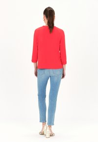Rote Bluse mit Dreiviertelärmeln, kombiniert mit hellblauen Skinny Jeans und beigen Blockabsatzsandalen. Glatte Stofftextur.