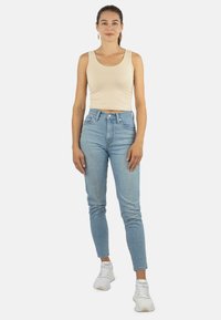 Beiger, kürzer geschnittener Tanktop, hoch geschnittene hellblauen Jeans, schmale Passform mit leichter Verwaschung und weißen Sneakers. Einfaches, lässiges Outfit-Design.