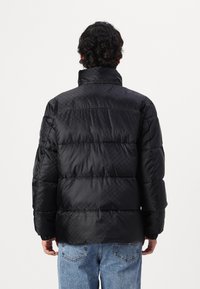 Chaqueta de plumas negra con un cuello alto, textura acolchada, que presenta puños elásticos y un dobladillo recto. Diseño moderno y ligero.