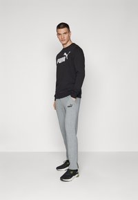 Fekete, hosszú ujjú póló fehér "PUMA" logóval, szürke melegítőnadrág, amelynek oldalán logó található, és fekete sportcipők zöld részletekkel.