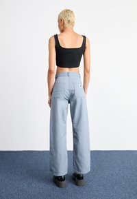 Top court noir à larges bretelles, associé à un pantalon large bleu clair avec deux poches arrière et un patch logo. Chaussures à plateforme noires.