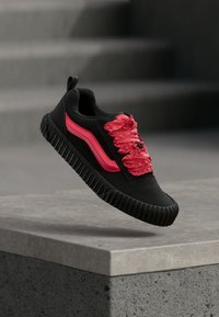 Baskets noires en tissu texturé, avec des lacets et des accents latéraux rose vif. Semelle en caoutchouc épaisse avec des rainures pour une meilleure adhérence.