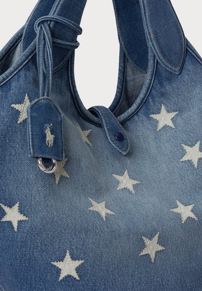 Torba z denimu z białym haftem w kształcie gwiazdy, zaokrąglonym kształtem, podwójnymi górnymi uchwytami oraz naszywką z logo i srebrnym okuciem.