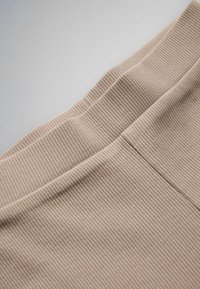 Close-up af beige ribbet stof med en søm, der går diagonalt over den strukturerede overflade.