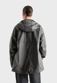 Chaqueta impermeable gris oscuro con capucha, que presenta un ajuste holgado y oversized, textura suave y detalles cosidos. Vista trasera mostrada.