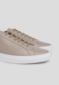 Zapatillas de piel beige con un acabado liso, que presentan suelas de goma blanca redondeadas, seis ojetes y cordones a juego. Diseño minimalista.