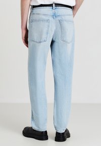 Jeans en denim bleu clair avec une coupe fuselée, dotés d'une taille standard, de deux poches arrière et d'une légère décoloration de la texture.