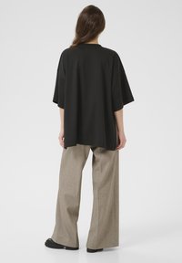 Sort oversized t-shirt med korte ærmer, rund halsudskæring, parret med lysebrune bredbenede bukser og sorte flade støvler.