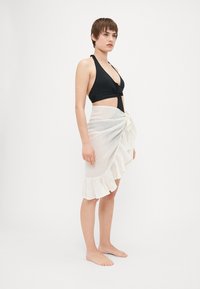 Črn halter bikini top z vozlom spredaj, v kombinaciji z belo laneno srajco s nabranim robom in zavezanimi pasom.