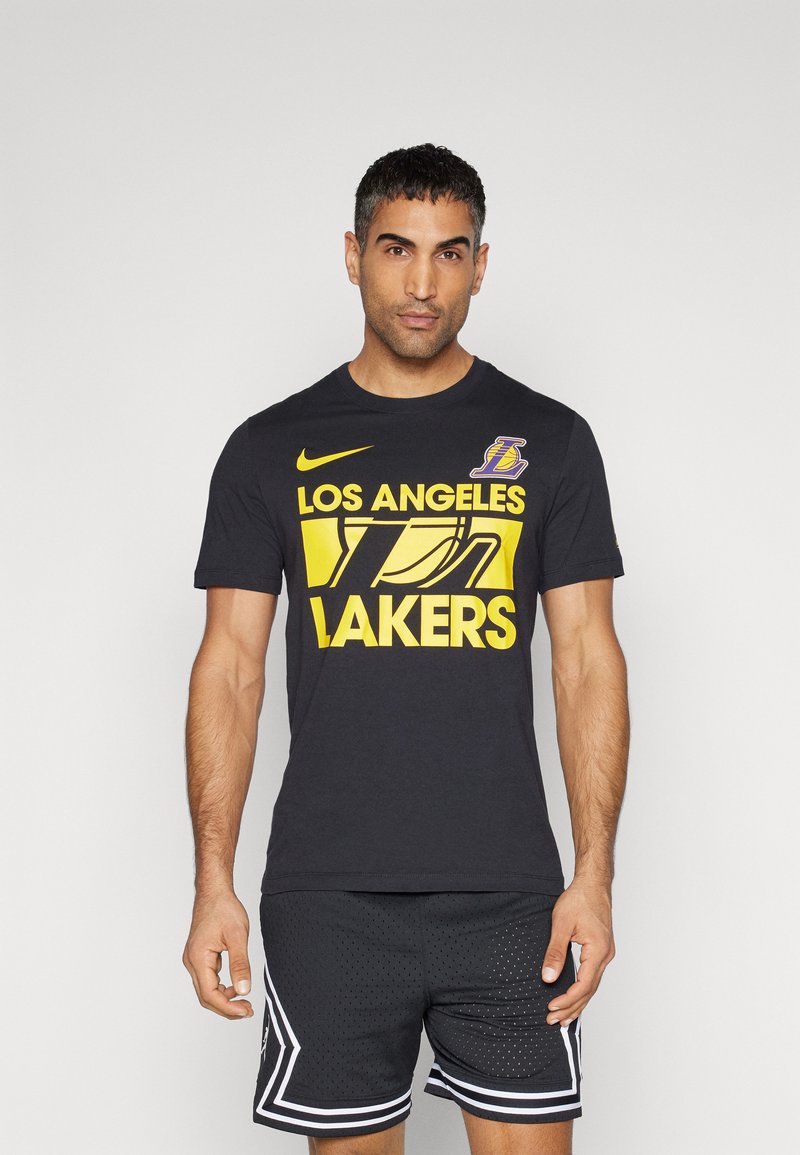 Camiseta de algodón negra con "LOS ANGELES LAKERS" en letras amarillas en negrita y un logo de los Lakers, combinada con pantalones cortos perforados negros.