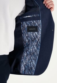 Marinblå skräddarsydd kavaj med mönstrad inredning i blått och svart, med en ficka som har en svart "BURATTI" etikett och kontrasterande s ömnadsdetaljer.
