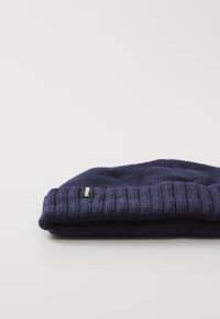 Námořnická pletená čepice s ribbed manžetou, vyrobená z texturované vlněné směsi, s malou černou logovou etiketou na boku.