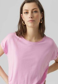 Rožinė trumpas rankovė t-shirt iš minkštos medžiagos, su laisvalaikio siluetu ir apvaliu iškirpimu, dėvima su dideliais auksiniais auskarais-žiedais.