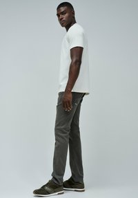 Camiseta blanca de cuello redondo, pantalones ajustados grises y zapatillas de deporte verde oscuro. Tejido suave y líneas limpias con detalles mínimos.