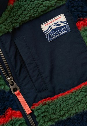 Buzunar bleumarin cu fermoar și sigla Joules Outdoor Apparel pe un material fleece texturat verde, roșu și albastru.