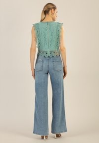 Helles türkisfarbenes Spitzenoberteil mit gewellten Kanten und einem Reißverschluss, kombiniert mit weiten blauen Jeans, die über Gesäßtaschen verfügen.