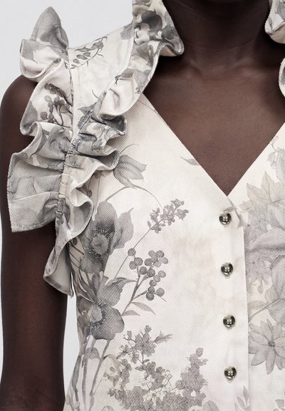 Φόρεμα με V-λαιμόκοψη και κουμπιά μπροστά, γκρι floral μοτίβο και βολάν στα μανίκια σε άτομο με σκουρόχρωμο δέρμα.